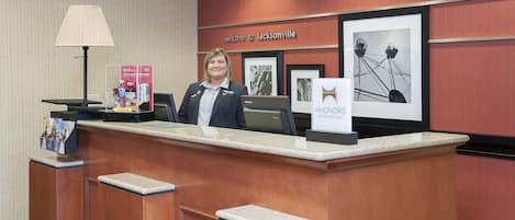 Una recepción con una mujer detrás, un cartel enmarcado que dice "Welcome to Jacksonville" y una imagen enmarcada de una noria.