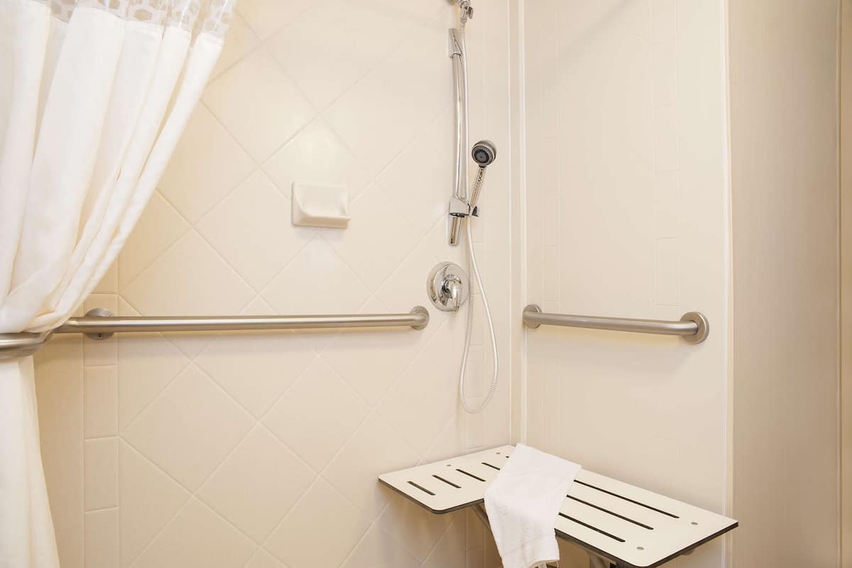 A shower with a handheld showerhead, grab bars, and a towel rack.