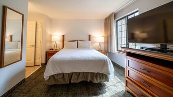 Quarto de hotel com cama, penteadeira, televisão e duas luminárias de cabeceira.