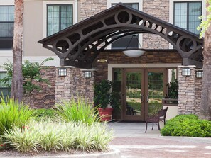A building entrance with a stone facade, a metal archway, and a bench. - Staybridge Suites Houston West / Energy Corridor by IHG (Houston)