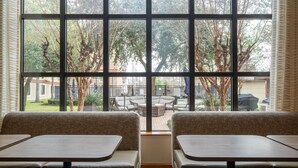 Un área de estar con mesas y bancos, ventanas amplias con vistas a muebles de exterior y árboles.