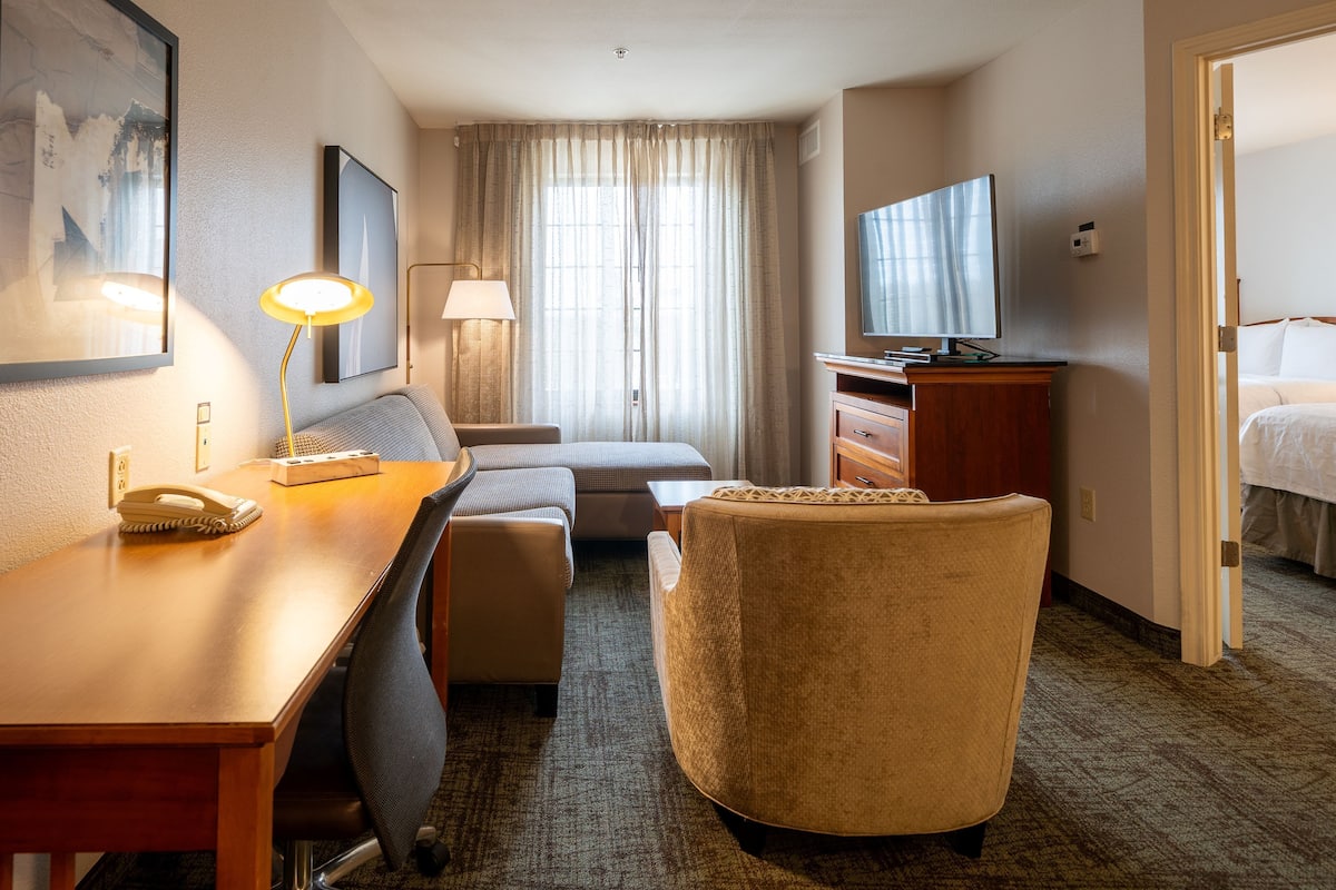 Ein Hotelzimmer mit Schreibtisch, Stuhl, Sofa, Fernseher und einem Bett.