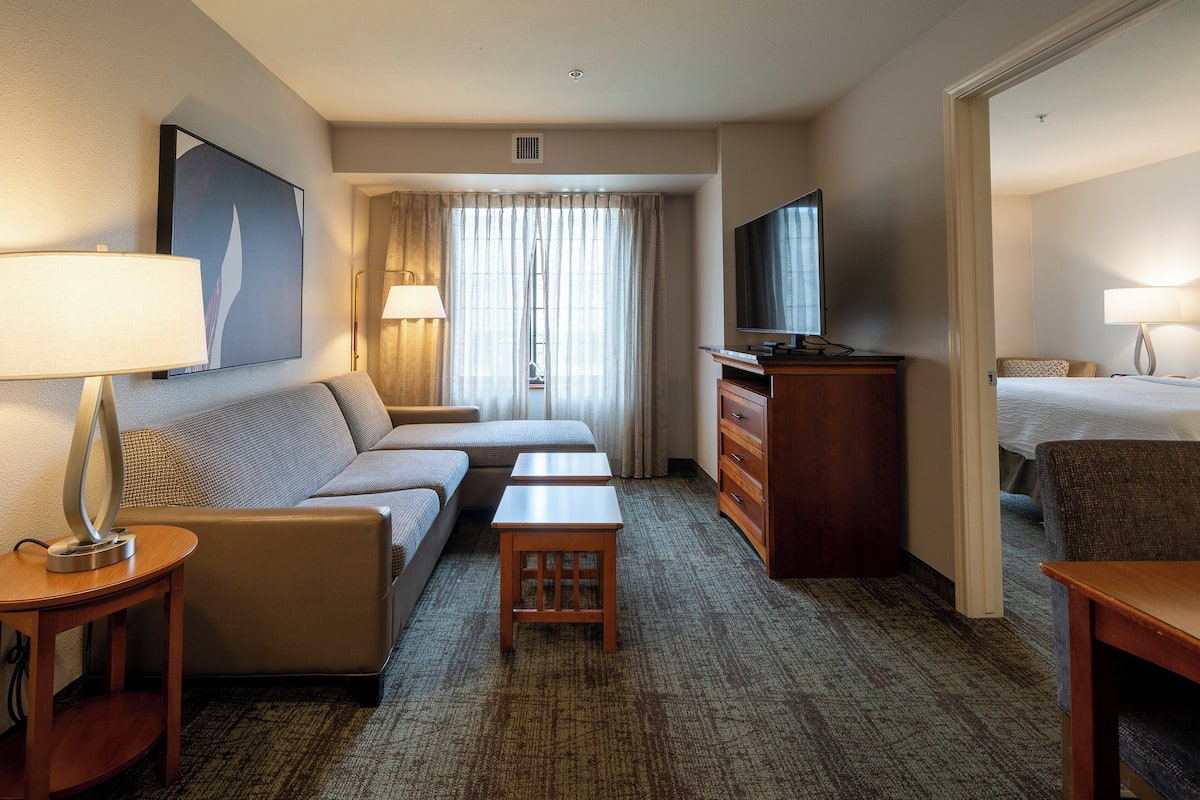 Ein Hotelzimmer mit einer Couch, einem kleinen Tisch, einem Schminktisch, einem Fernseher und einem Bett.