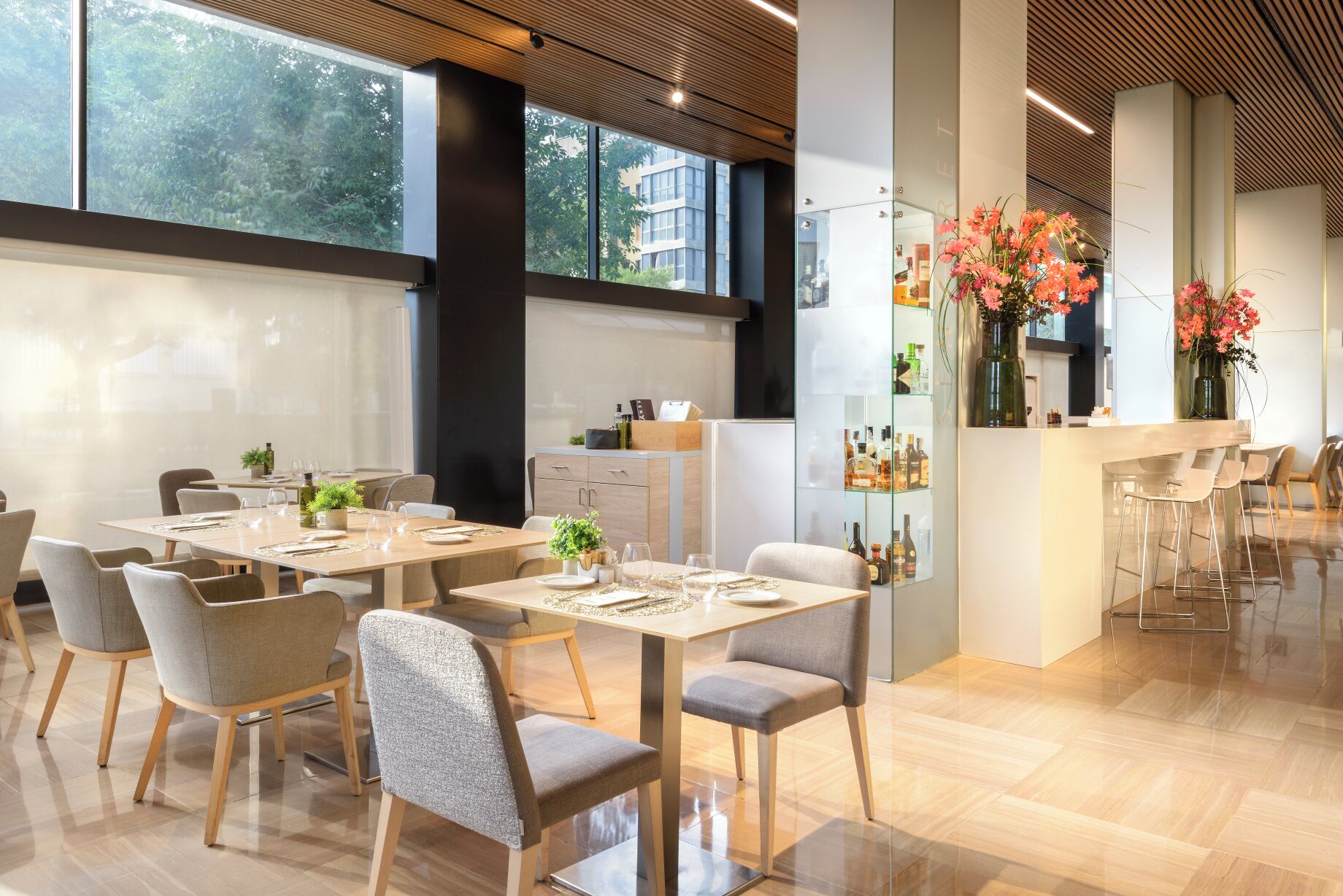 Un espace repas moderne avec plusieurs tables et chaises, un coin bar avec des tabourets et une vue sur la ville grâce à de grandes fenêtres.