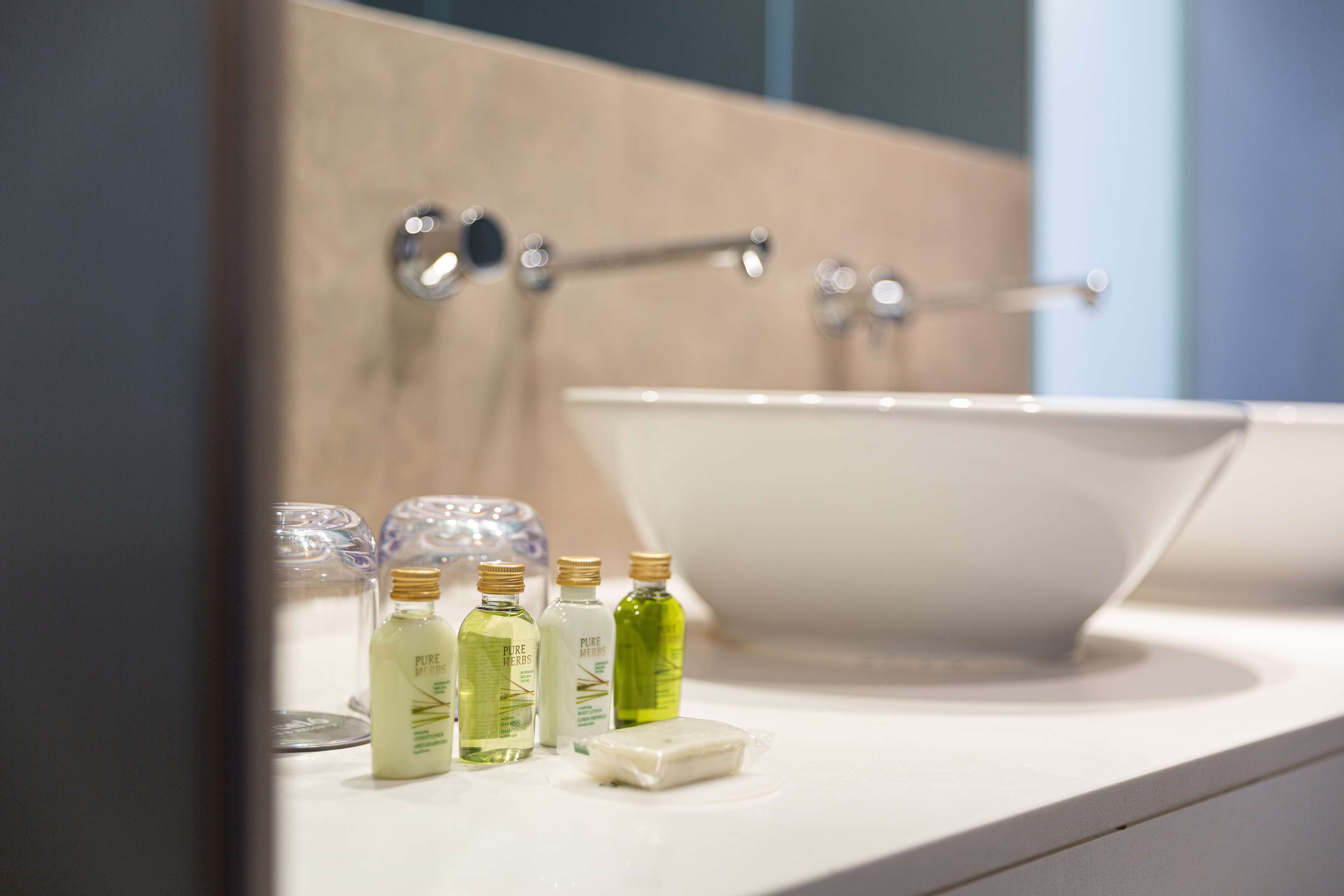 A bathroom with a white sink, a mirror, and three bottles of liquid soap on the counter.