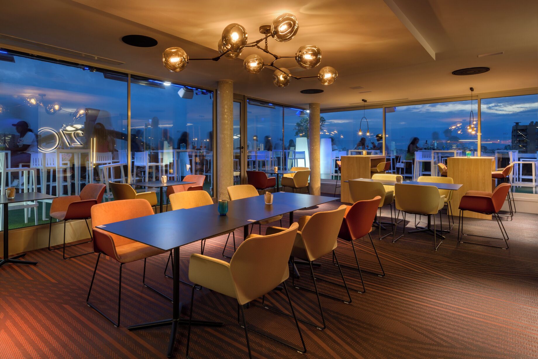 A conference room with tables and chairs, large windows, and a modern chandelier.