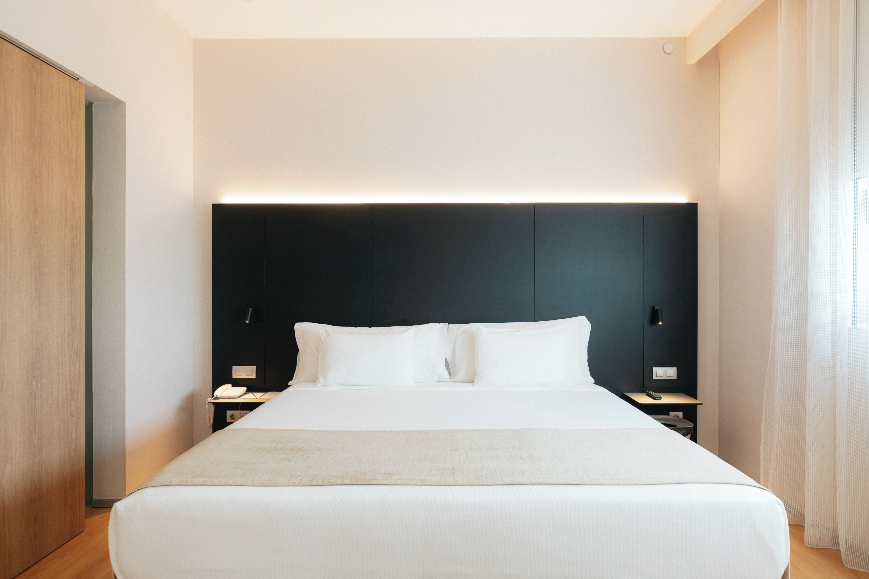 Een moderne hotelkamer met een groot bed, nachtkastjes en een donker hoofdeinde.