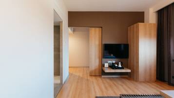 Un dormitorio moderno con suelo de madera, un televisor de pantalla plana montado en la pared, una mesita de noche con lámpara y un armario grande.