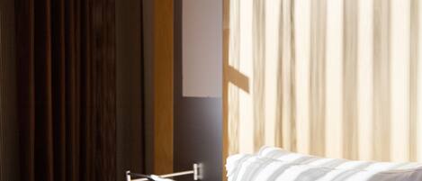 A hotel room with a bed, a wooden door, and a large window with curtains.