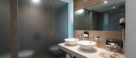 A modern bathroom with two white sinks, a large mirror, and a shower area.