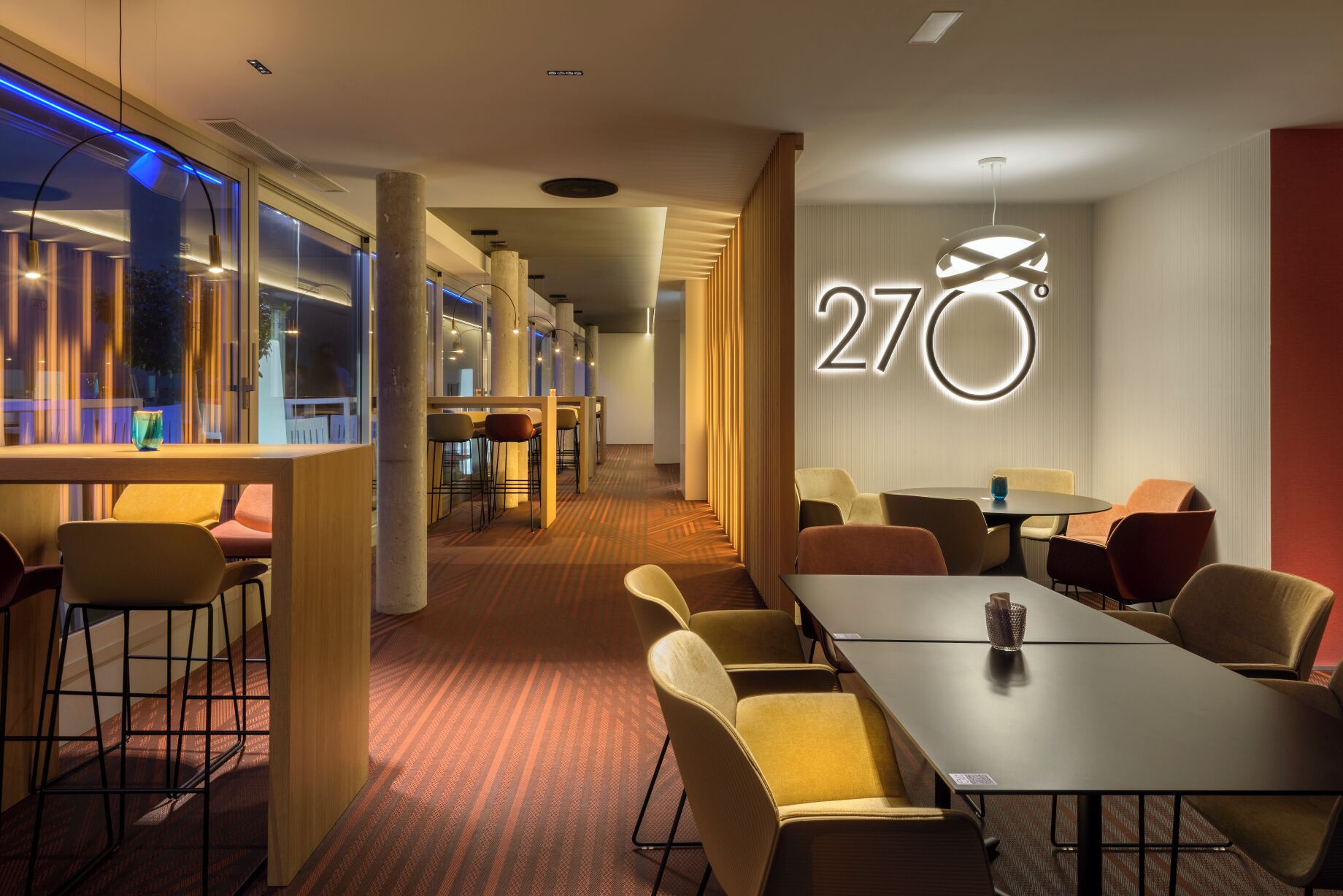 Vestíbulo de hotel con mostrador de recepción, zona de estar y un llamativo letrero con el número '270'.