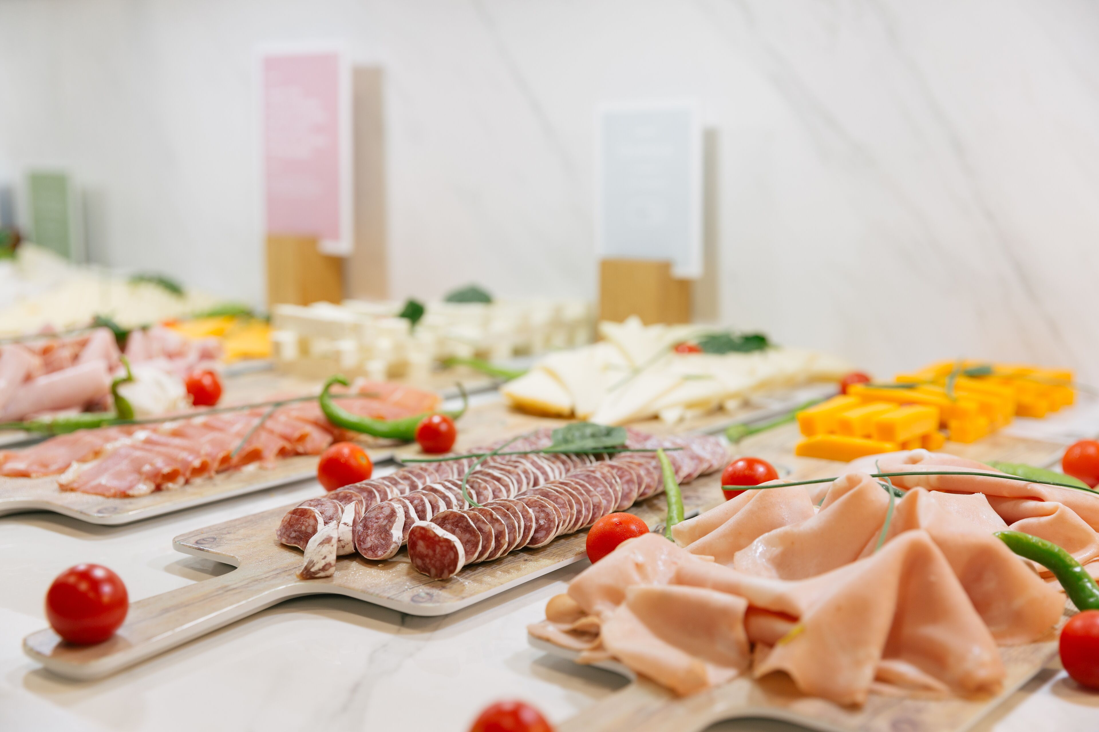 A variety of meats and cheeses arranged on wooden boards, with cherry tomatoes and green peppers as garnish.