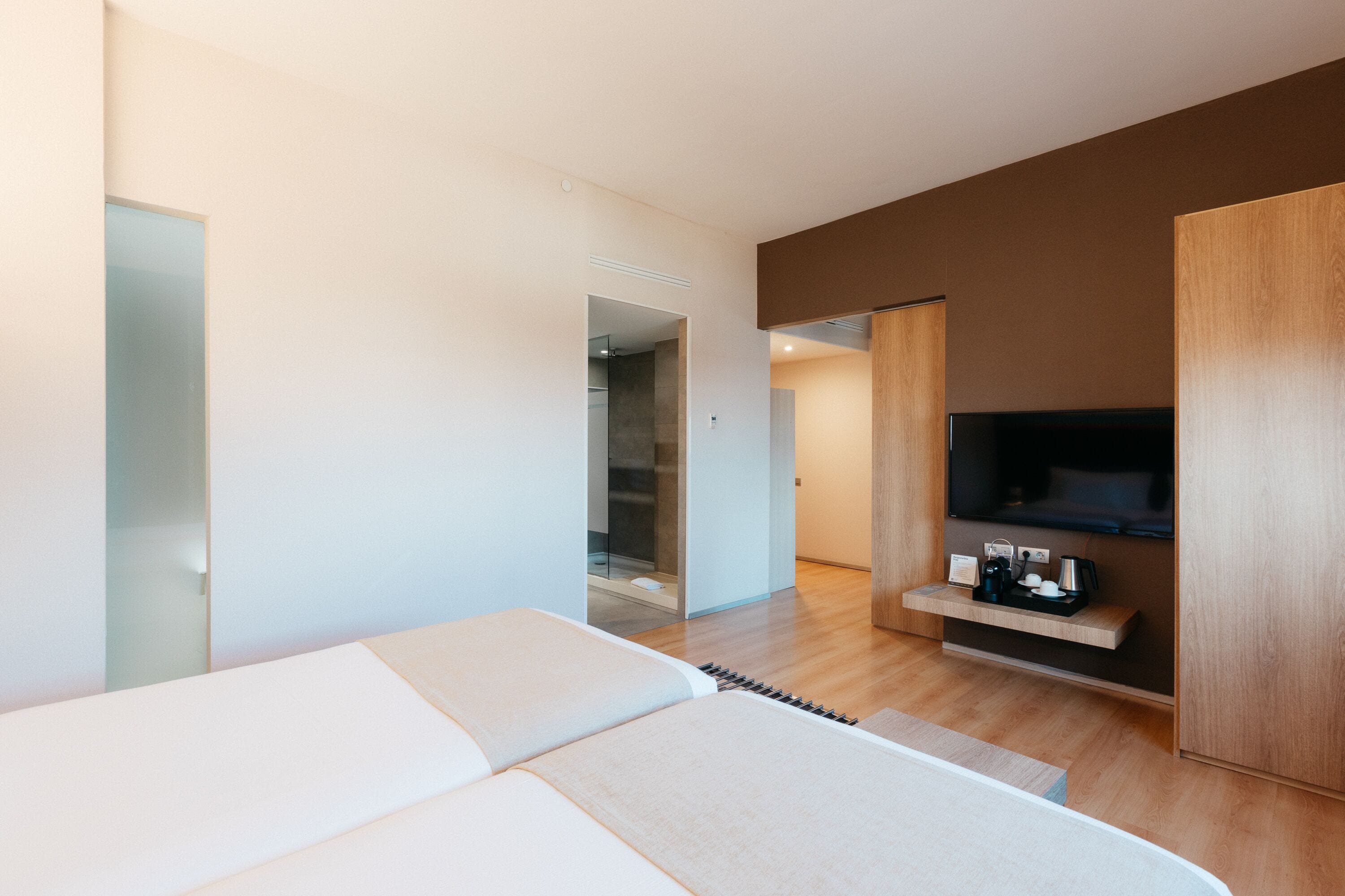 Ett modernt hotellrum med en stor säng, en TV och en liten hylla med diverse föremål.