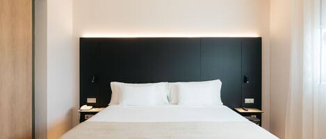 Una habitación de hotel moderna con una cama grande, mesitas de noche y un cabecero oscuro.