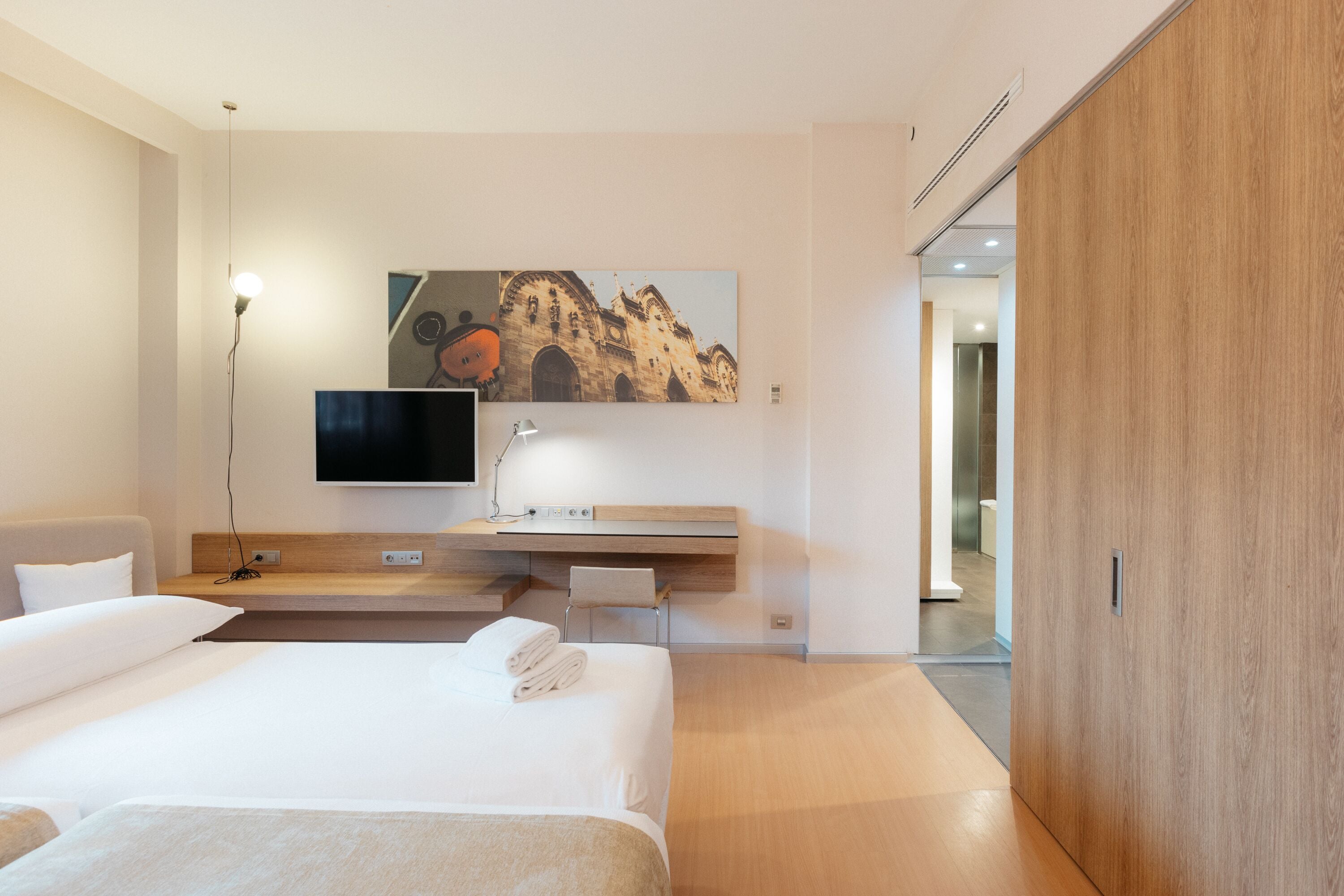 Ein modernes Hotelzimmer mit einem großen Bett, einem flachbildfernseher an der Wand, einer Holzeinrichtungsplatte und einem großen Fenster.