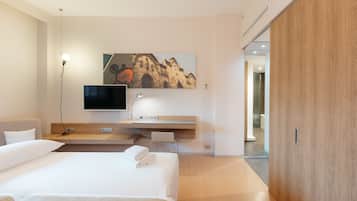 A modern hotel room with a large bed, a flat-screen TV mounted on the wall, a wooden vanity, and a large window.