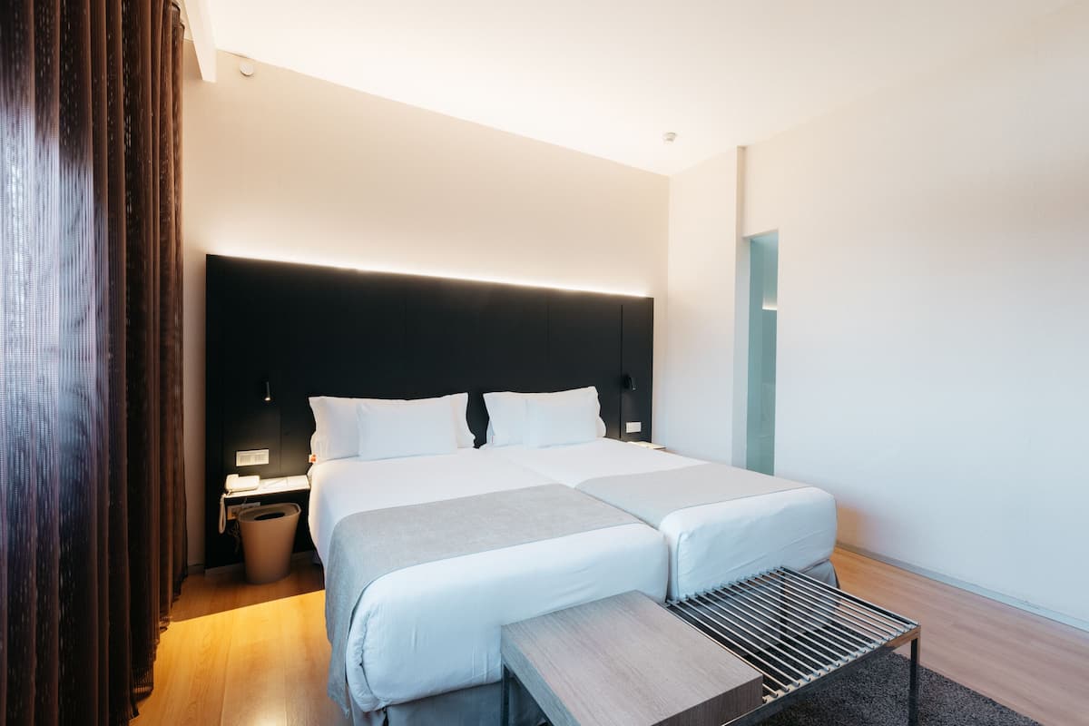 Moderni hotellihuone, jossa on suuri sänky, yöpöydät, penkki ja tumma pääty.