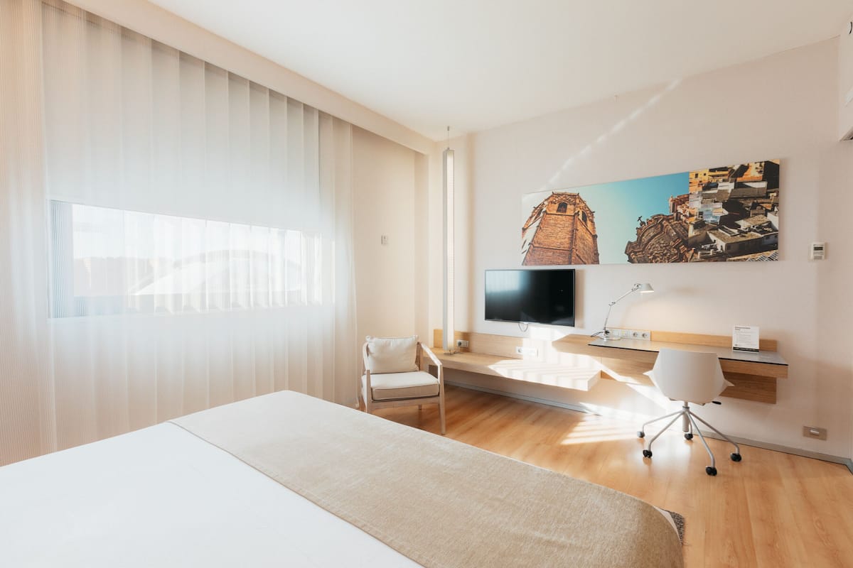 Moderni hotellihuone, jossa on suuri sänky, työpöytä, jossa on tietokone, tuoli ja televisio.
