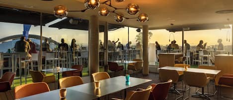 A modern dining area with tables and chairs, a unique spherical light fixture, and large windows offering a city view.