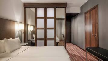 A hotel room with a bed, a desk, a chair, a wardrobe, and a bench.