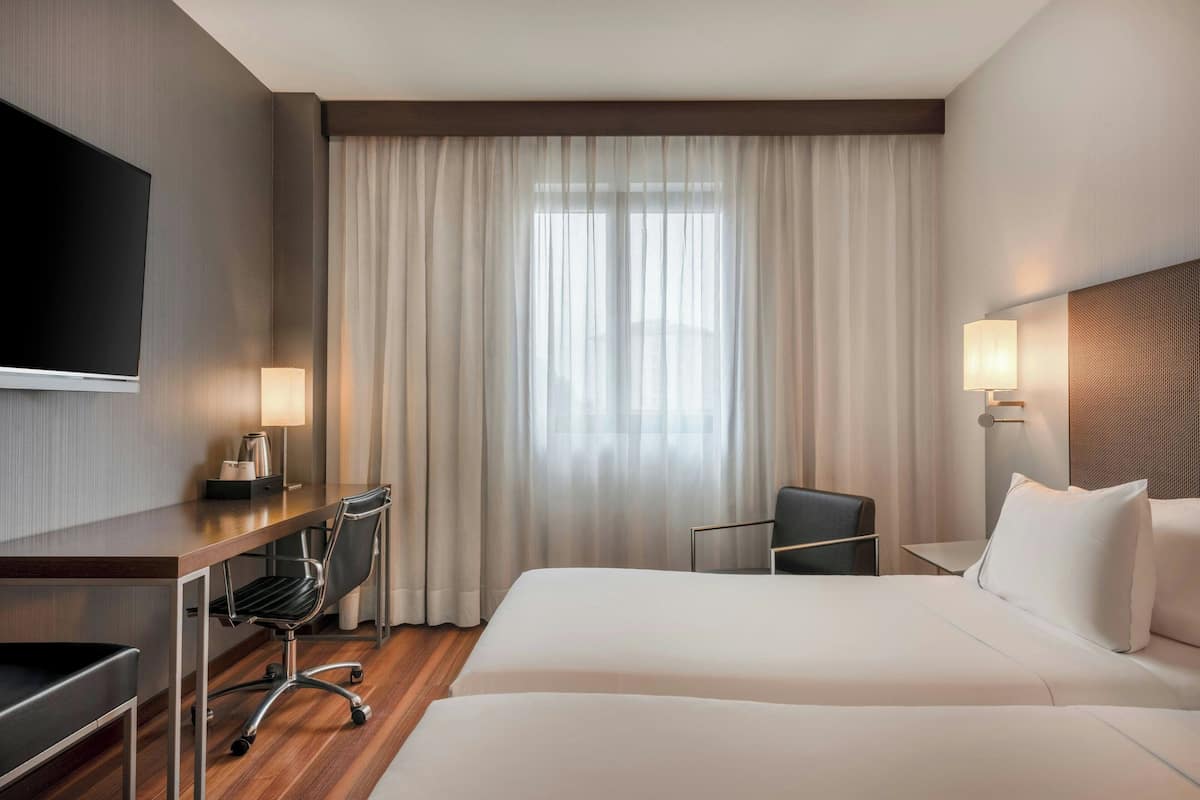 A hotel room with a bed, a desk, a chair, a TV, and a window with curtains.