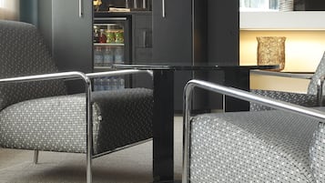 Ein modernes Wohnzimmer mit einem dunkelgrauen Sofa, einem runden Tisch und einer integrierten Küche mit Regalen und einem Kühlschrank.