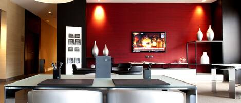 A modern hotel lobby with a reception desk, seating area, and a television displaying a news channel.