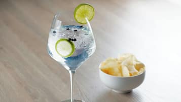 A clear glass with ice and a lime slice, a bowl of chips, and a wooden surface.