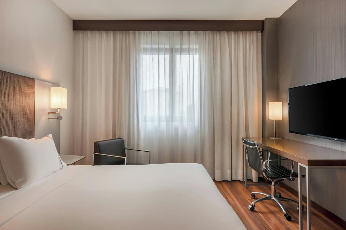 A hotel room with a large bed, a desk with a chair, a TV, and a window with curtains.