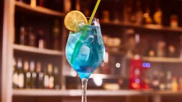 A cocktail glass with a blue drink, a lemon slice, and a straw on a bar counter.