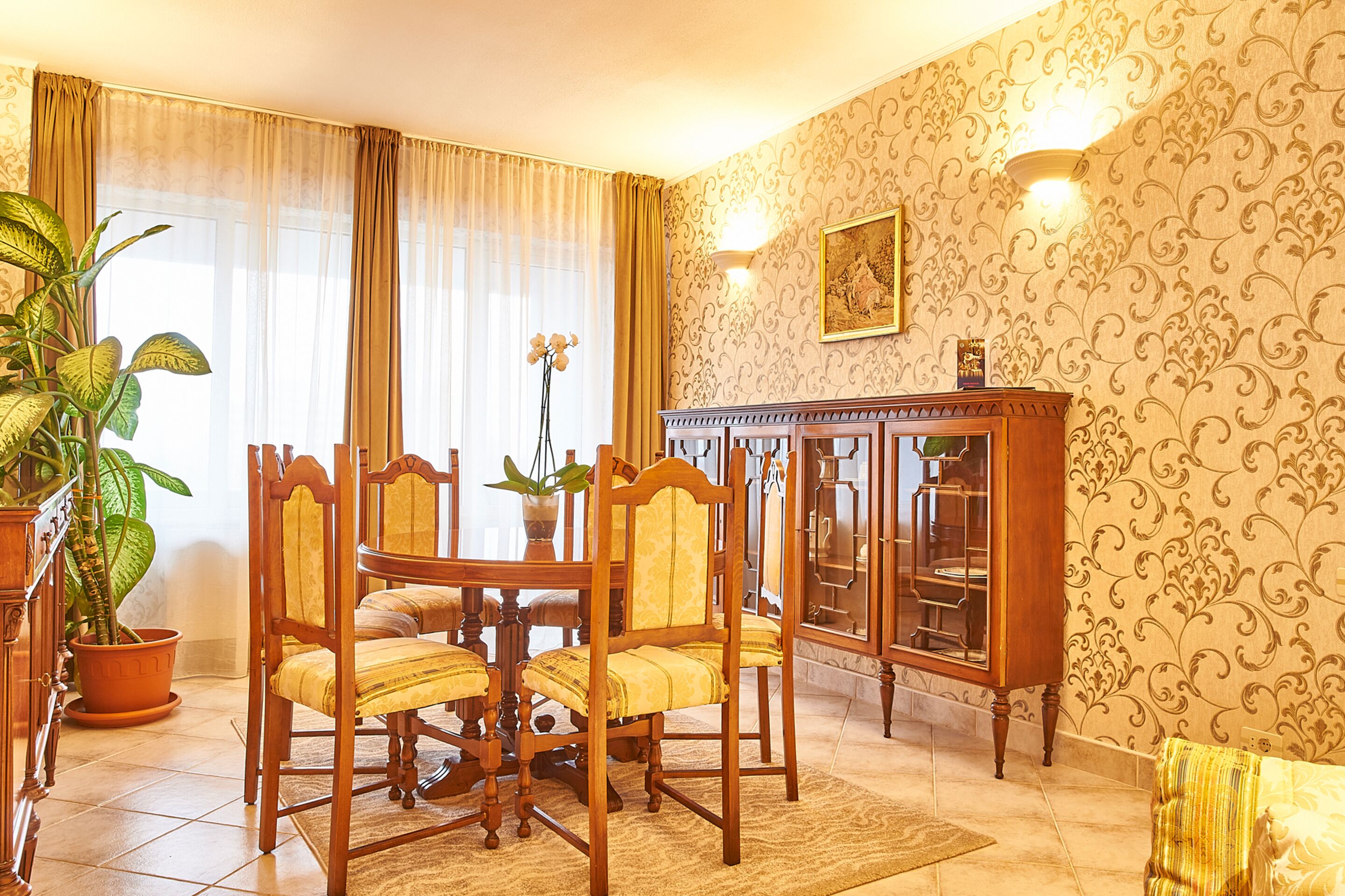 Un comedor con mesa y sillas de madera, una planta en maceta y un mueble con puertas de vidrio.