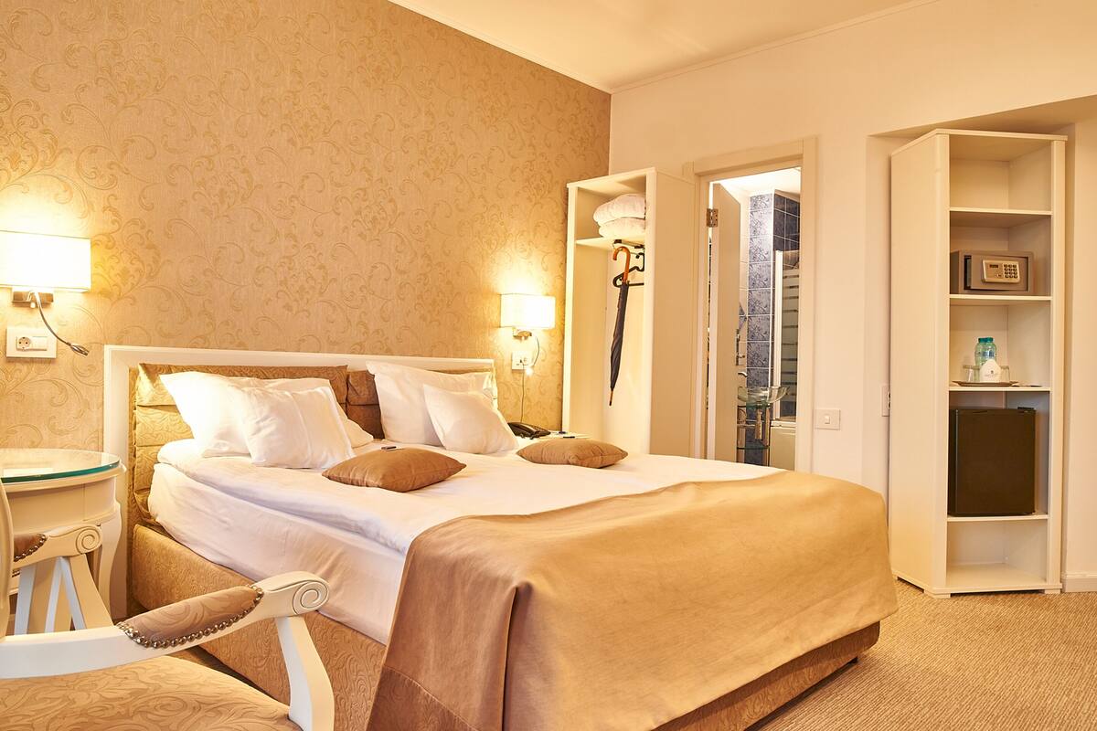 A hotel room with a large bed, bedside lamps, a small table, and a chair.