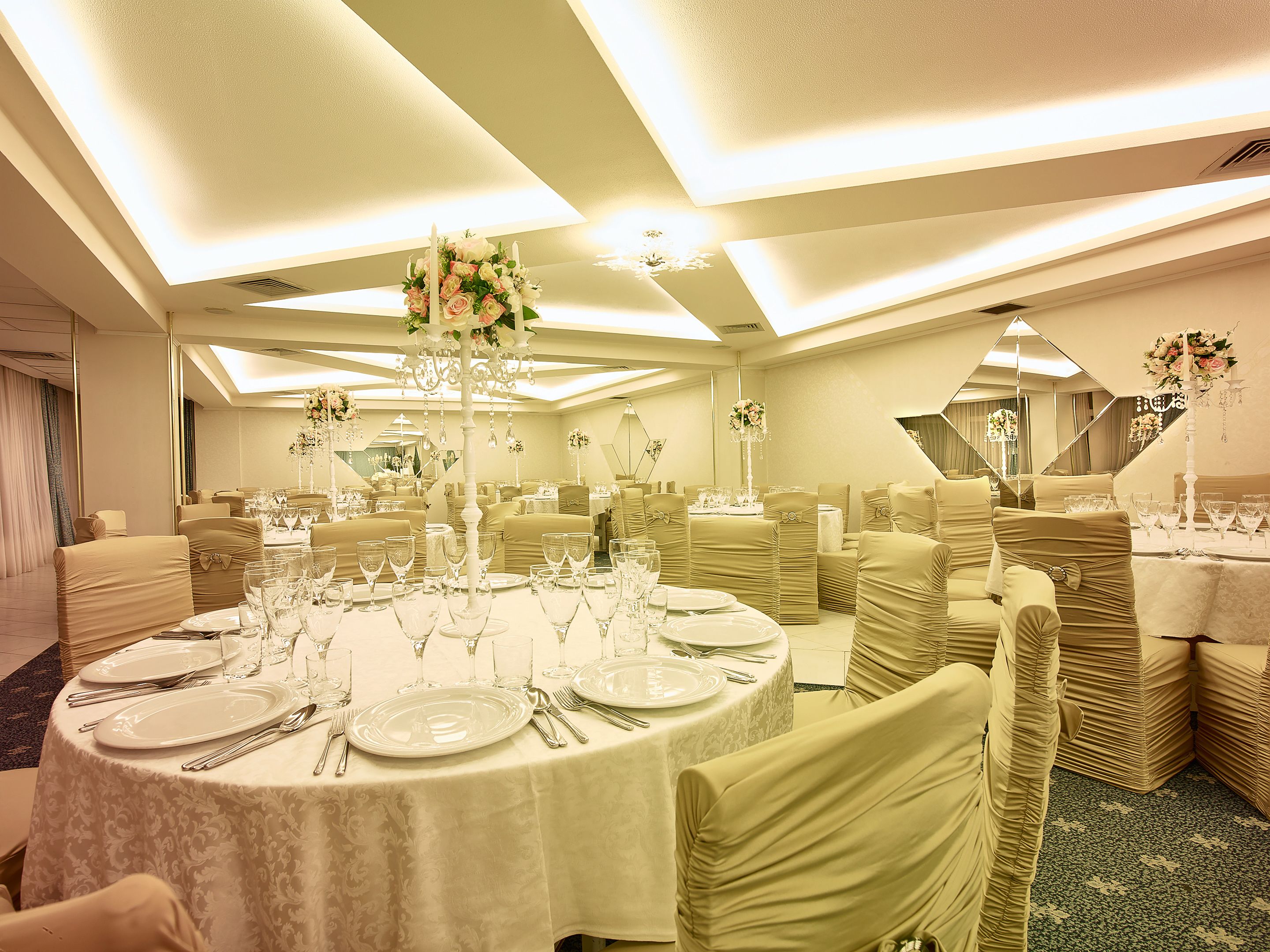 A banquet hall with round tables, chairs, and floral centerpieces.