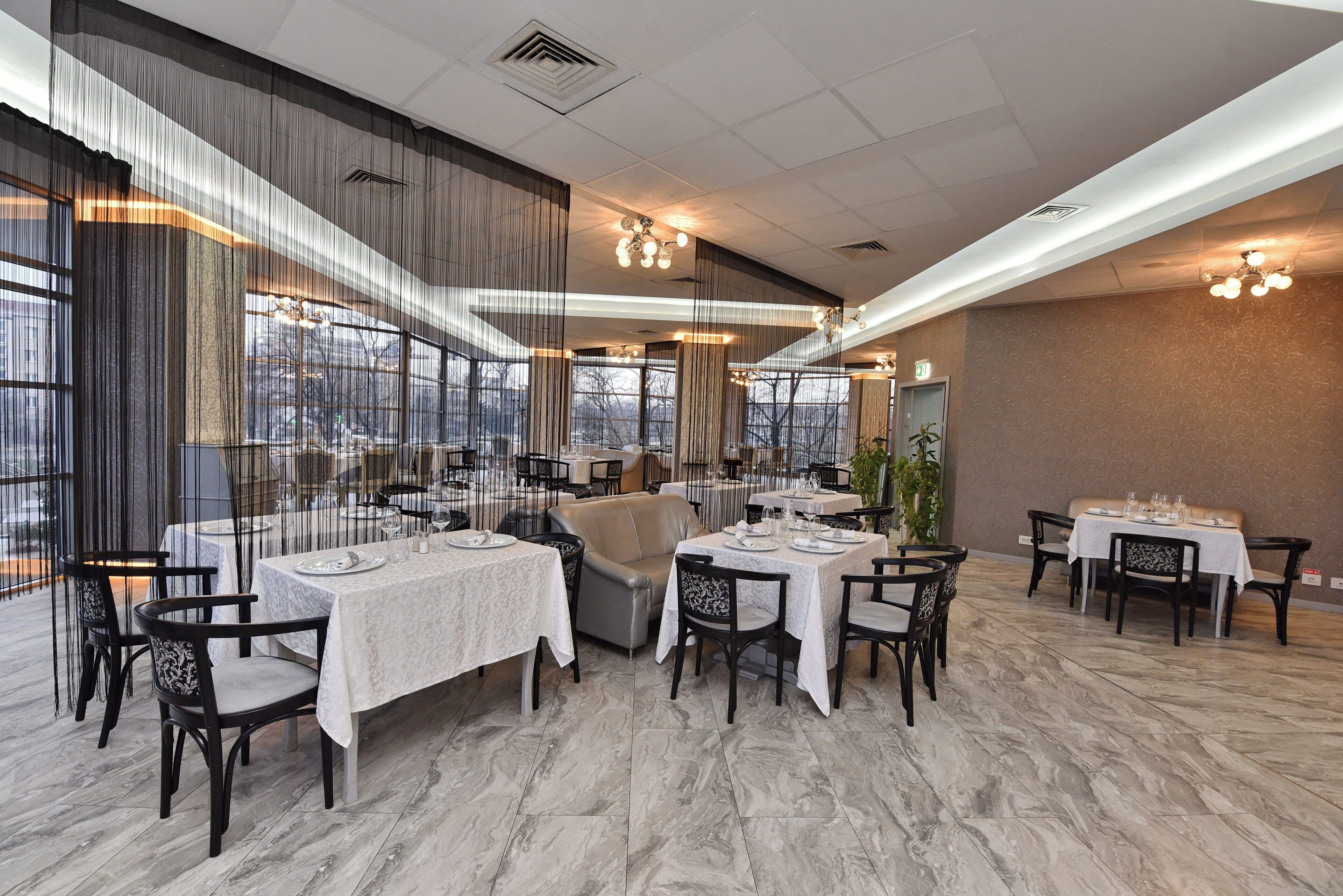 Un restaurant avec des tables dressées pour le service, de grandes fenêtres et une vue sur l’extérieur.