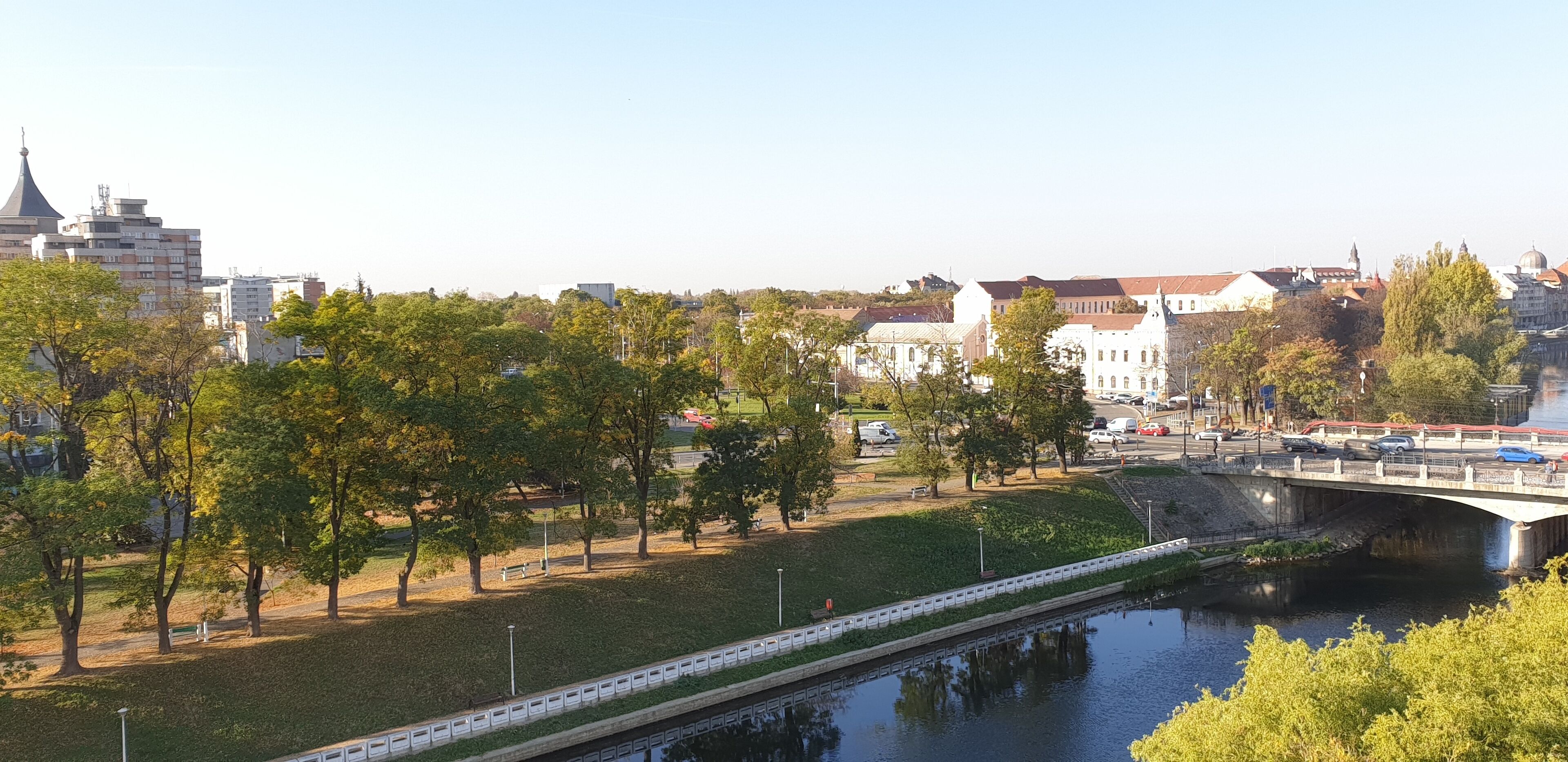 A riverside park with trees and a bridge over a river.