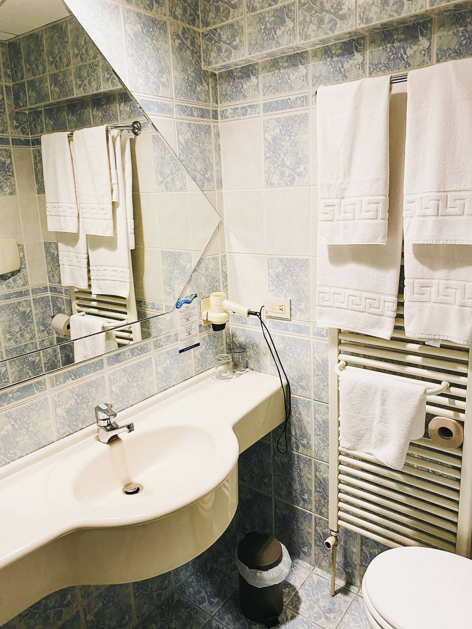 Un baño con lavamanos, espejo, toallero y retrete.