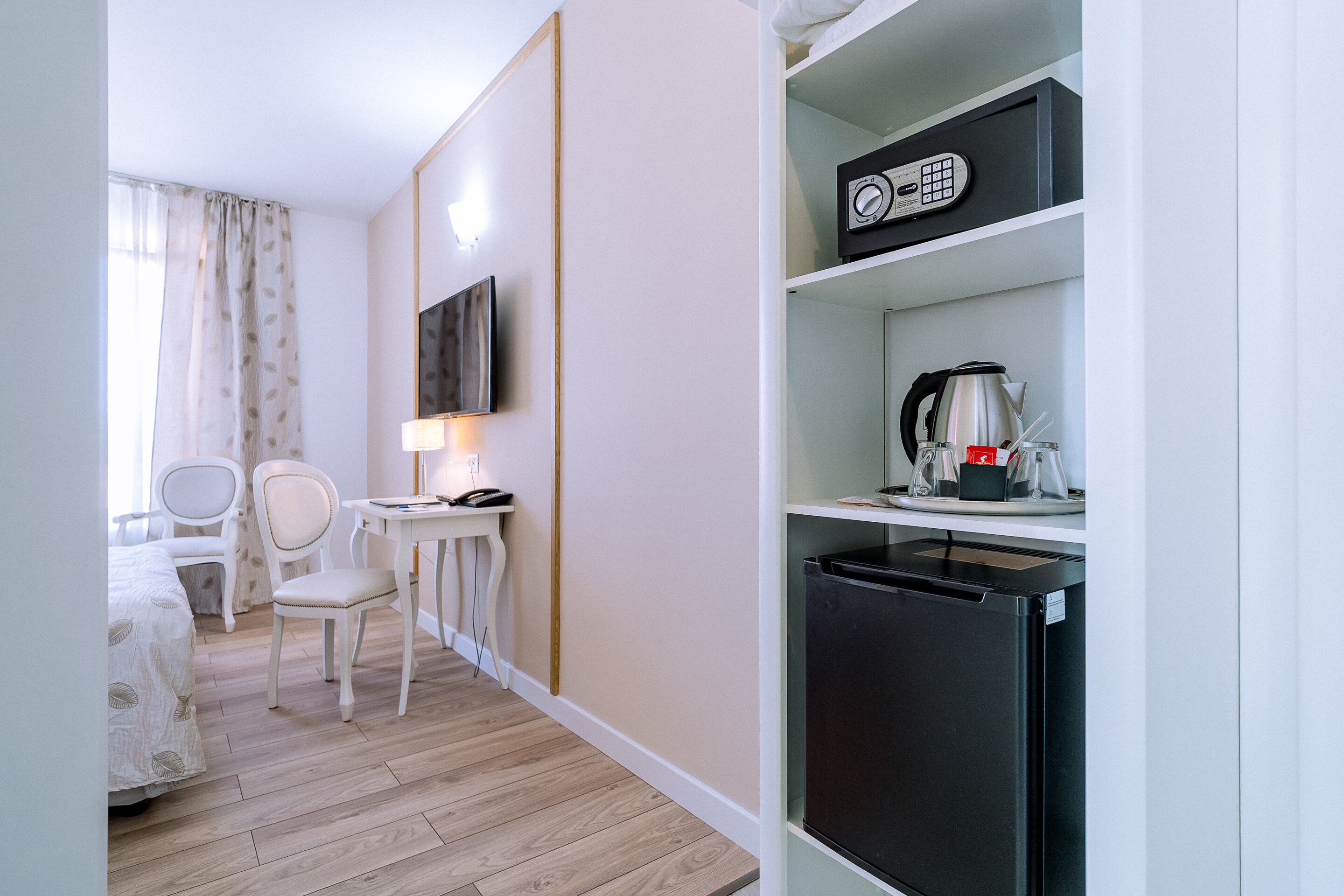 Une chambre d’hôtel équipée d’un lit, d’un bureau avec une lampe, d’une chaise, d’une télévision, d’une machine à café et d’un mini-réfrigérateur.