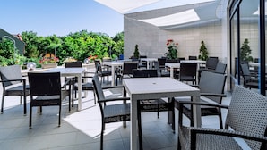 An outdoor patio with tables and chairs, surrounded by greenery and a tiled floor. - Continental Forum Oradea (Oradea)