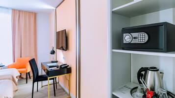 Habitación de hotel con escritorio, silla, cama y estante con cafetera y hervidor.