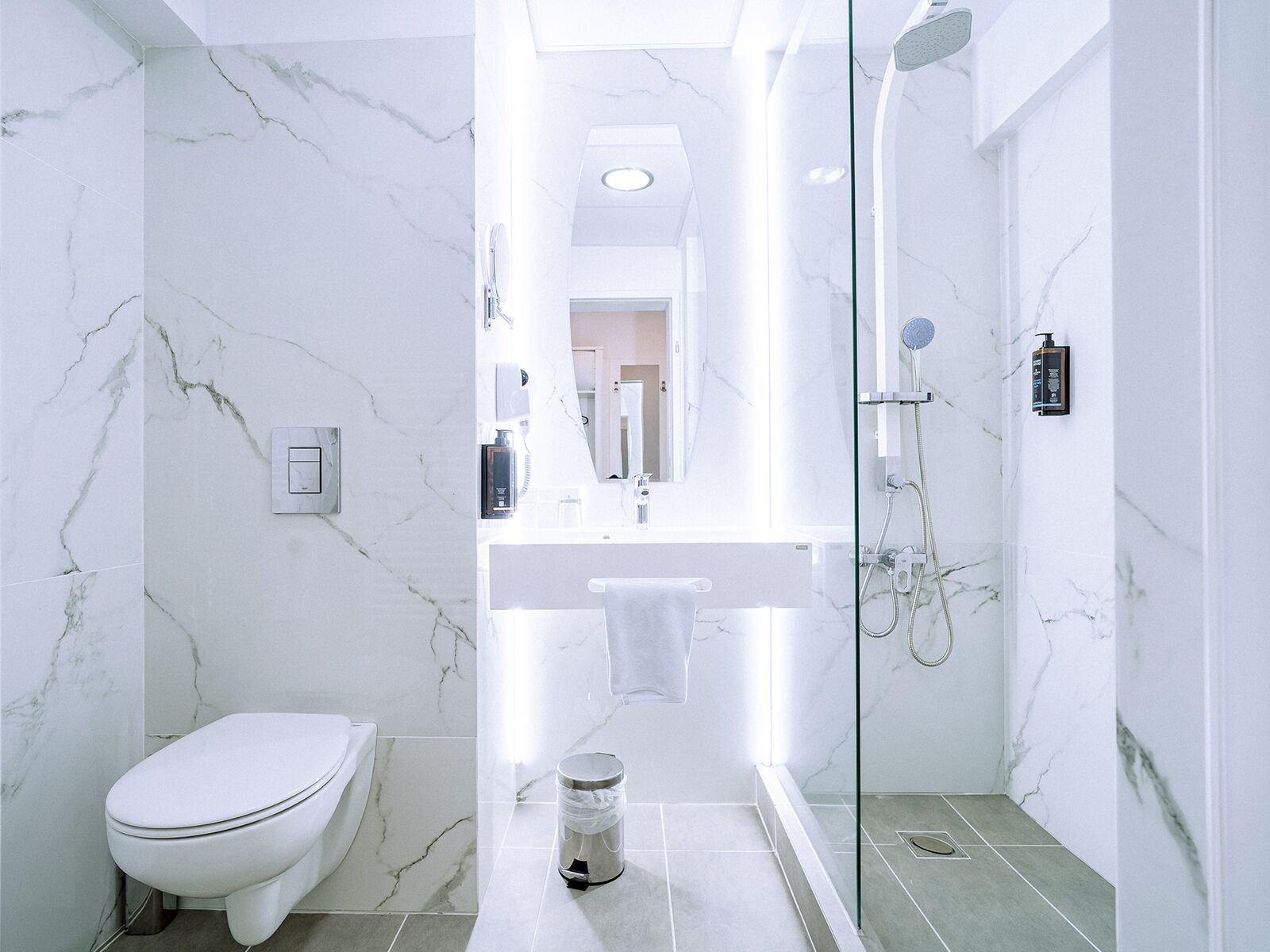 A modern bathroom with a toilet, a glass-enclosed shower, and a marble-tiled wall.