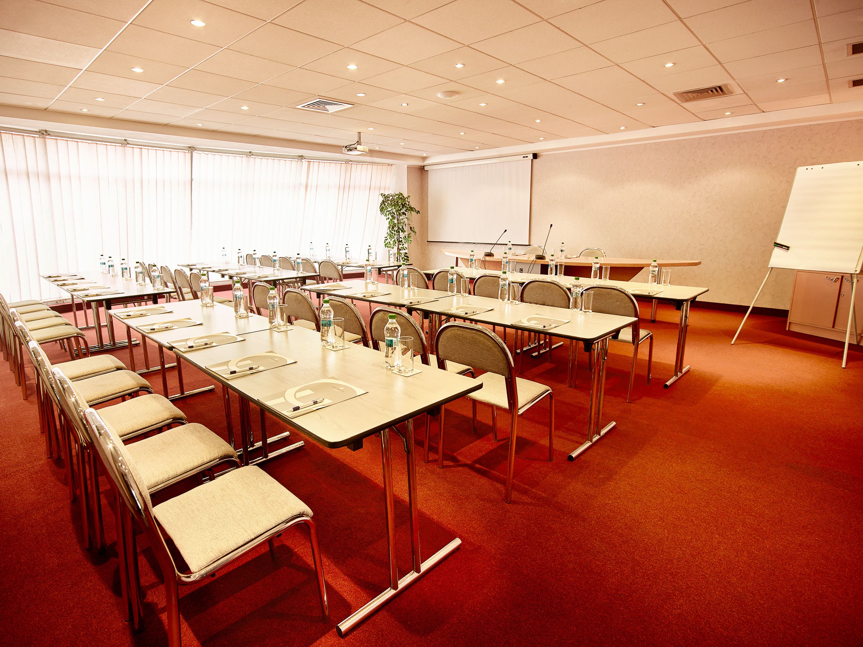 A conference room with multiple tables, chairs, and a projector screen.