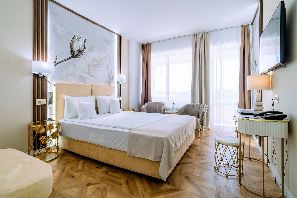 A hotel room with a large bed, a desk with a chair, a TV, and a window with curtains.