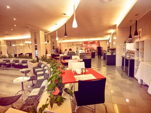 Eine moderne Hotellobby mit Sitzbereichen, einem Empfangstresen und einer Küche im Hintergrund.