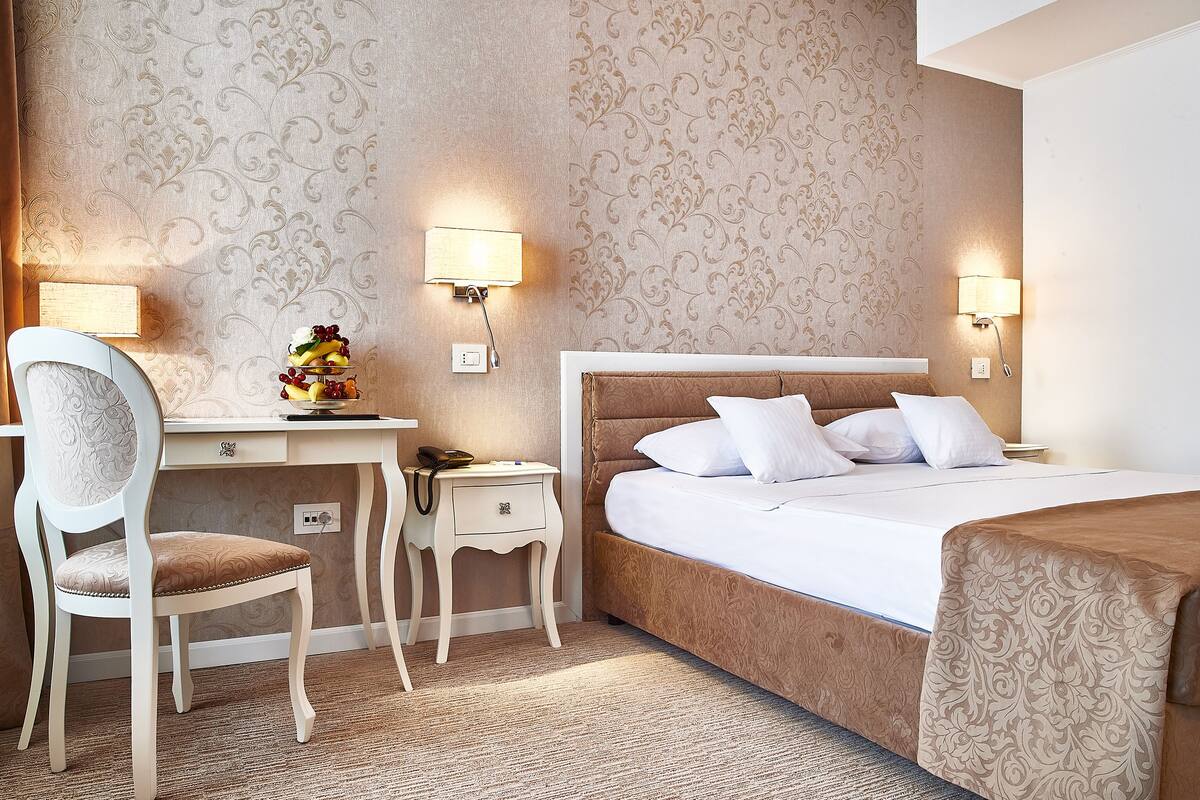 A hotel room with a bed, a desk, a chair, and two wall-mounted lamps.