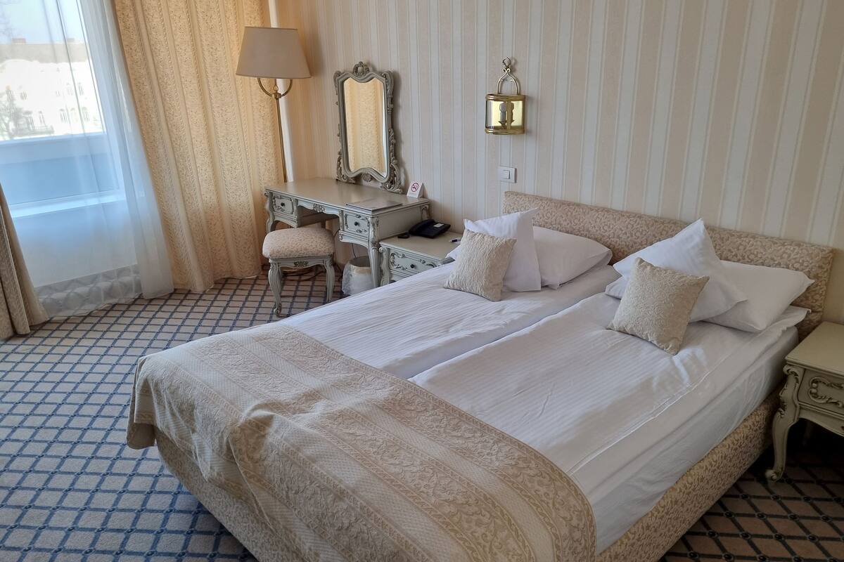 A hotel room with a large bed, a desk, a chair, and a lamp.