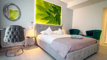 A modern bedroom with a large bed, a tufted armchair, and a green accent chair.