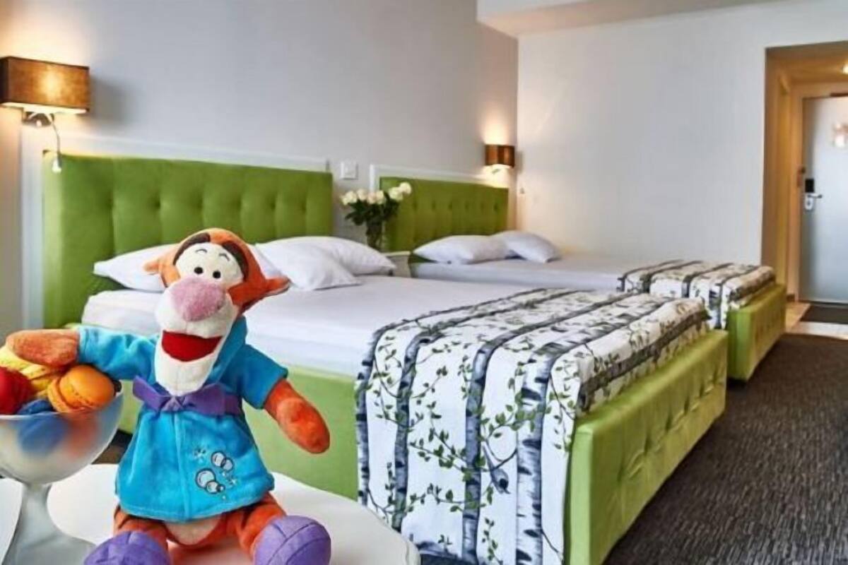 A hotel room with a green upholstered headboard, a bed with white bedding, and a plush toy on a side table.