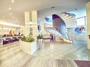 A modern hotel lobby with a central staircase, seating areas, and a reception desk. - Hotel Continental Forum Arad (Arad)