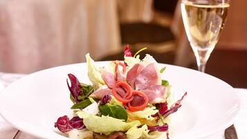 A white plate with a salad, a glass of white wine, and a knife on a table.