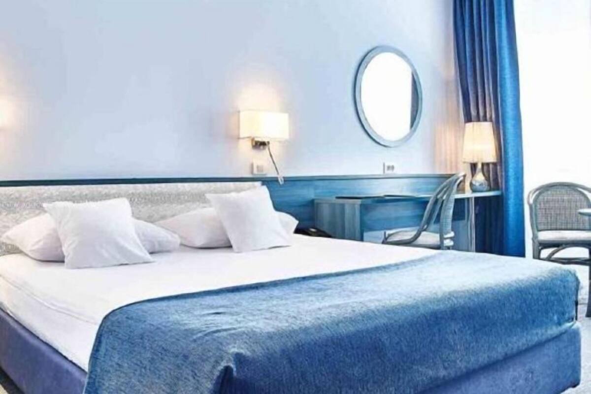 A hotel room with a bed, a desk, a chair, a round mirror, and a window with curtains.